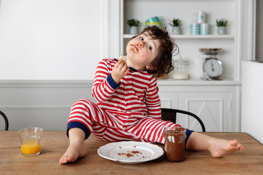 Toddler with chocolate smeared face eating slice of bread