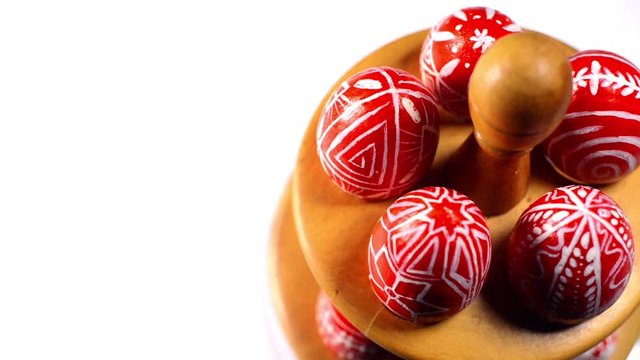 Red easter eggs with folk Ukrainian pattern lay and revolve on wooden stand for eggs which stand on white background. Ukrainian traditional eggs pisanka and krashanka.
