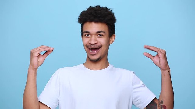 Fun african american young guy 20s in white t-shirt curly hair posing showing blah blah gesture ja jaja hands isolated on blue background studio portrait. People sincere emotions, lifestyle concept