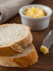 Duas fatias de pão em uma mesa de madeira e uma faca com manteiga