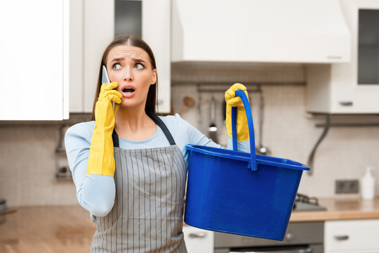 Scared young woman calling plumber holding bucket