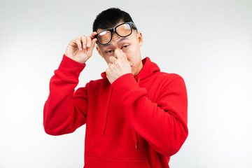 stylish brunette Asian man in a red sweater and glasses for vision rubs his eyes on a white background