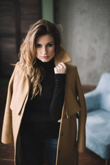Beautiful sexy woman with curls and full lips in a beige coat in a loft style studio. Beauty and fashion. Soft selective focus.