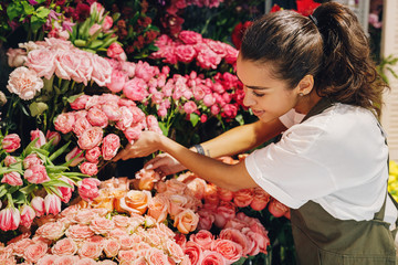 Young woman working in a flower shop. Female florist choosing flowers. - obrazy, fototapety, plakaty