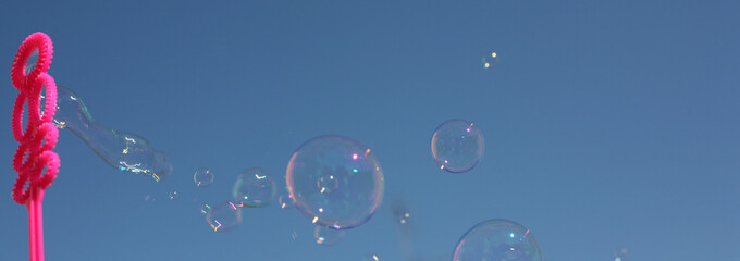 blowing soap bubbles with pink stem in a blue sky