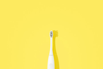 Electronic toothbrush on yellow pastel background.