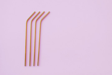 Reusable eco-friendly golden metal straws on pastel pink background.