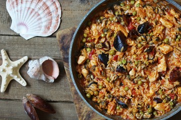 paella from orzo pasta with mussels, seashells and chicken. Seafood paella, traditional spanish dish. Paella on rustic black wooden table. Top view
