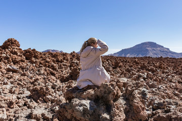 young blond girl sitting on the stone in teide national park, volcanic landscape, view of...