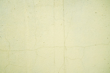 Old cracked light yellow colored concrete wall, weathered building background.