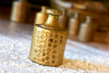 Old copper or brass scale weights with calibration marks on wooden table with flour in a bakery. Image with selective focus.