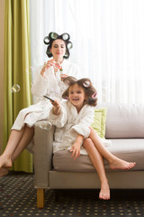 Mom and daughter  in white bathrobes with curlers in their hair Make manicure and pedicure at home....