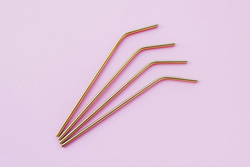 Reusable eco-friendly golden metal straws on pastel pink background.