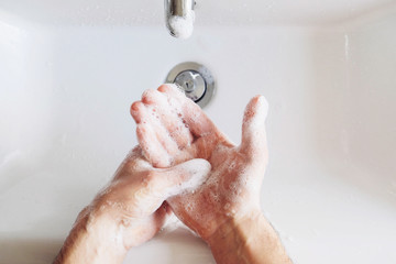 Man cleaning his hands using liquid disinfectant soap and water in bathroom.