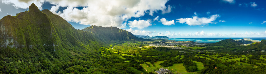 A Panoramic aerial image from the Pali Lookout on the island of Oahu in Hawaii.  With a bright green rainforest, vertical cliffs and vivid blue skies. - obrazy, fototapety, plakaty