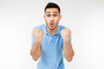 Fototapeta premium handsome Caucasian in a blue T-shirt rejoices victory holding his fists on a white studio background