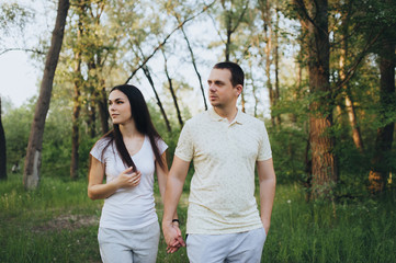 Obraz premium Loving, beautiful, stylish guy and girl in tracksuits strolling through the forest, holding hands, outdoors in the park. Love story newlyweds. Photography, concept.
