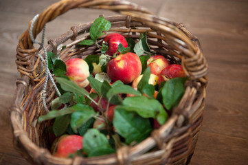 A wicker basket full of red ripe apples with green leaves stands on a wooden table .  the view from the top The concept of harvest 2020. crisis in the agro-industry