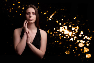 Teenage Girl with long hair and hands close to face in black top on black background with lights