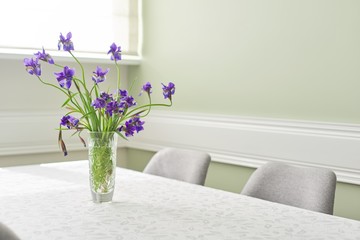 Bright dining room interior, table and chairs near window, bouquet in vase