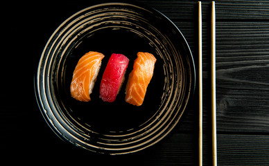salmon and tuna sushi on a black plate and a black wooden background