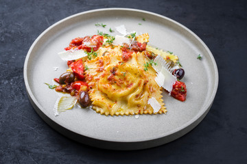 Traditionelle italienische Ravioli Pasta angeboten mit Parmesan Käse, gebratene Tomaten und Oliven als closeup auf einem Modern Design Teller
