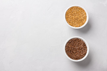 Golden and brown raw flax seeds in white bowls on a gray textured background, top view, space. healthy vegan superfood
