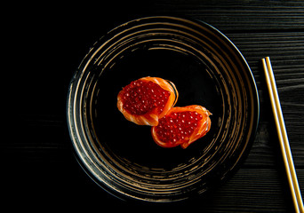 delicious sushi with salmon and red caviar on a black plate and a black wooden background