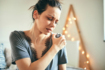 Woman suffering from shoulder pain while sitting on bed.