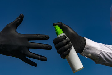 Unrecognizable person in black gloves applying sanitizer spray on the hands on blue background. Precautionary measures at COVID-19. Coronavirus ncov Protection Concept.