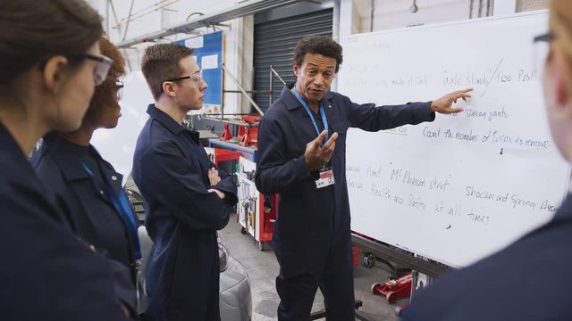 Male tutor by whiteboard with students teaching auto mechanic apprenticeship at college - shot in slow motion