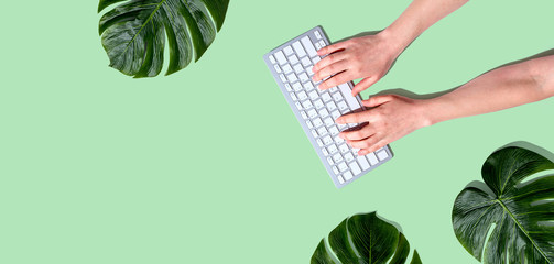 Person using a computer keyboard with tropical leaves from above - obrazy, fototapety, plakaty