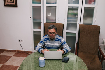 Senior man using a computer at home. Telecommuting during quarantine. Communication with family members during confinement. Selective focus.