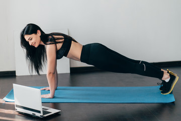 Home training, fitness, motivation concept. Young fit woman doing sport exercises with online guide...