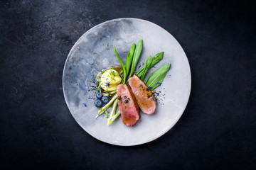 Traditional gourmet duck breast filet with mashed potatoes and ramson leaves in orange sauce as top view on a modern design plate with copy space