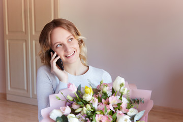 Young blonde girl talking phone bouquet of flowers as a gift. Flower delivery birthday gift for women.