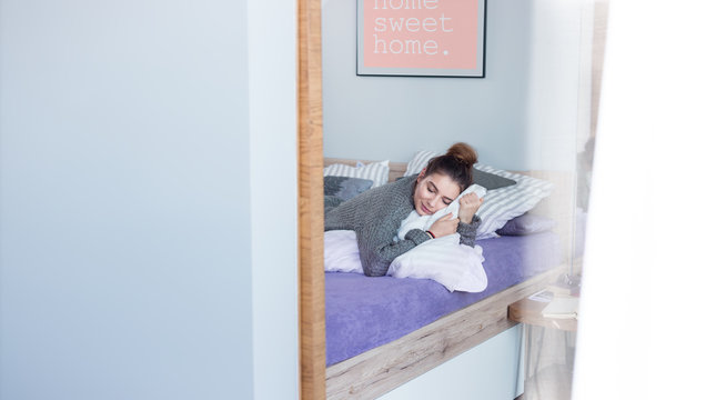 Young, beautiful woman waking up from a nap with "home sweet home" poster on the wall. Lifestyle image, copy space.
