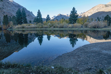 Fototapeta na wymiar reflecctive mountain lake with pines aspens grass and mountain