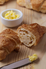 Croissant cortado e uma faca com manteiga sobre mesa de madeira