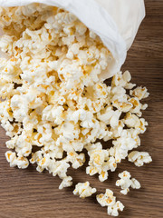 Saco de pipoca caído sobre mesa de madeira com pipocas espalhadas