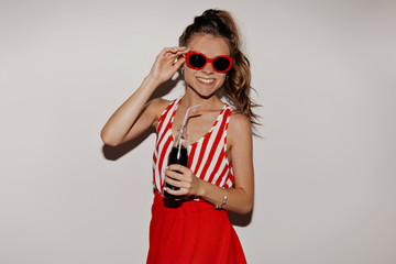 Lovable pretty girl wearing red trendy glasses and red skirt posing with charming smile with coke posing over isolated background