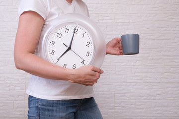 Woman freelancer with clock showing 7 am and a cup of coffee, punctuality during remote and distant...