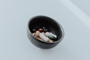 Bowl of vitamins or supplements in a black bowl on white background