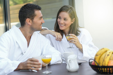 Obraz na płótnie Canvas Happy young couple in bathrobes having breakfast outdoors