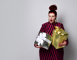 Plus size model in striped dress, earrings. Holding golden and silver gift boxes, looking wild with joy, posing isolated on white
