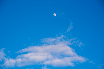 A bright Blue sky with thick white clouds and a white moon. Copy space for text, design.
