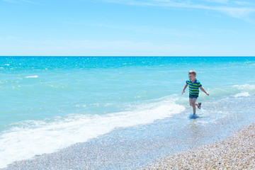 A little boy in a hat runs across the water on the sea, the ocean. The concept of rest, vacations.