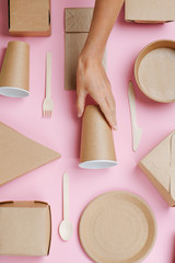 Female hand placing cup in the middle of eco-friendly dishware composition