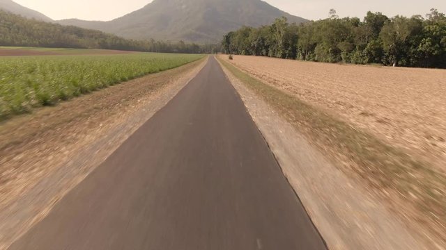 Beautiful mountain landscape with sugar cane fields. Dramatic DRONE aerial view of fields, trees, green forest, farm, mountains, blue sky & road. Walsh's Pyramid, Cairns, Australia.
