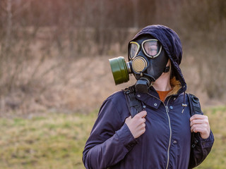 COVID-19. Girl in a black gas mask and dark clothes with a hood at sunset on a background of spring...